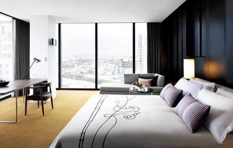 Crown Metropol Melbourne Hotel Exterior foto The photo depicts a modern hotel room that features a stylish and contemporary design. 

- **Bed**: There is a large bed with decorative pillows and an elegantly designed bedspread.
- **Seating Area**: Next to the bed is a gray sofa that complements 