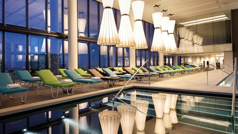 Crown Metropol Melbourne Hotel Exterior foto The photo shows a modern, stylish indoor pool area with large windows that provide a view of the city. The room is beautifully lit by distinctive, large pendant lights that hang from the ceiling. Alongside the pool, there are several lounge chairs in