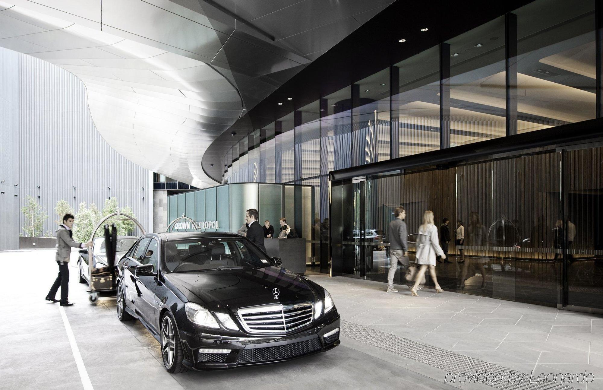 Crown Metropol Melbourne Hotel Exterior foto The image depicts a modern urban setting with a sleek, black luxury sedan parked in front of a sophisticated building. The architecture features clean lines and a combination of glass and metallic elements. In front of the entrance, there are people 