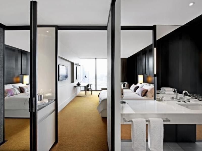 Crown Metropol Melbourne Hotel Exterior foto The photo shows a modern hotel room with a stylish and sleek design. The space is divided by glass and panel partitions, creating a sense of openness. 

On one side, there is a large bed with soft linens and decorative pillows, accompanied by bedside