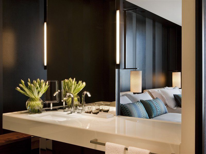 Crown Metropol Melbourne Hotel Exterior foto The photo shows a modern interior space that appears to be a blend of a bathroom and a living area. In the foreground, there's a sleek, white countertop with a sink and faucets. Two vases of fresh, vibrant flowers are positioned on one side. In the b
