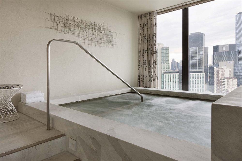 Crown Metropol Melbourne Hotel Exterior foto The photo features a modern indoor hot tub or spa located near a large window with a view of city skyscrapers. The tub is rectangular and has a metallic safety railing. The surrounding area is designed with sleek, neutral-colored materials, and there